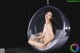 A naked woman sitting in a hanging chair.