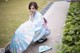 A woman in a blue kimono sitting on the ground with an umbrella.