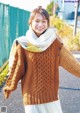 A woman wearing a brown sweater and a white scarf.