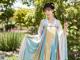 A woman in a blue and yellow hanbok standing in a garden.